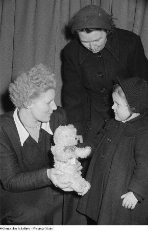 Eine Verkäuferin im Handelsorganisation-Kaufhaus präsentiert einer Frau und einem Kind einen Teddybär