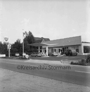 BP-Tankstelle: Hamburger Straße: Neubau: rechts Gebäude: davor Zapfsäulen mit tankenden Pkws und Kleintransporter: links BP-Schild und parkende Pkws: dahinter Bäume und Wohnhäuser