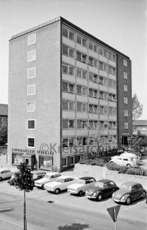 Hochhaus [später Gebäude B]: Mommsenstraße: Blick vom Bahnhofsgebäude: vorn Kreisparkplatz und Pkws: hinten Hauptgebäude [später Gebäude A] und Garagentrakt