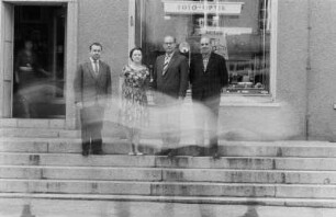 Niesky. Mehrere Personen (Lehrer oder Dozenten ?) auf den Stufen vor einem HO-Industriewarenladen "Foto - Optik"