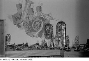 Verschiedene Blechblasinstrumente vor einem Wandbild musizierender Bergmänner auf der Leipziger Herbstmesse 1954