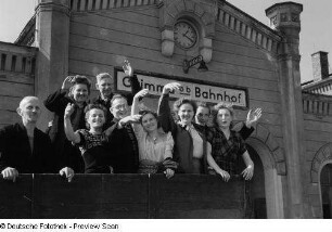 Winkende Erntehelfer vom VEB Mihoma auf einem Anhänger vor dem Bahnhofsgebäude