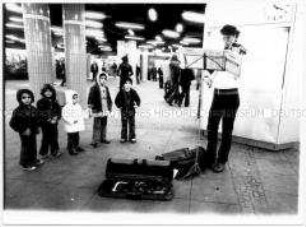Fünf Kinder hören einem Straßenmusiker zu (Altersgruppe 14-17)