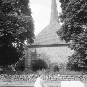 Friedenskirche: Außenansicht von Osten: vorn Felsteinwall mit Bewuchs: dahinter Kirchhof: rechts und links Bäume: im Vordergrund Fahrradfahrer