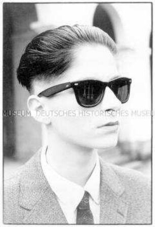 Porträt eines jungen Mannes mit nach hinten gegelten Haaren und schwarzer Sonnenbrille (Altersgruppe 18-21)