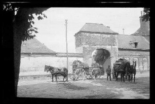 Origny (=Origny-Sainte-Benoite, Dep. Aisne, Frankreich): 2 Zweispänner mit Wagenkarren vor einem ummauerten Anwesen mit hohem Eingangstor (Distanzaufnahme)