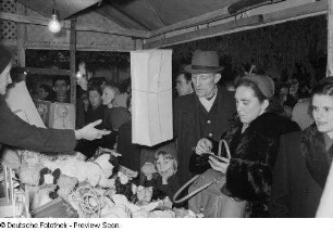 Verkaufsstand für Puppen und Spielwaren umringt von Besuchern auf dem Leipziger Weihnachtsmarkt bei Dunkelheit