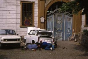 Trabantreparatur auf der Straße : Zwei Männer liegen auf der Straße und reparieren einen Trabant. Aufgenommenin Gera im Frühjahr 1990