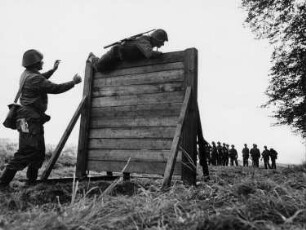 Überwinden einer Eskaladierwand. Ausbilder, Soldat und Gruppe in Wartestellung