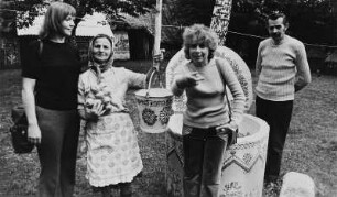 Drei Frauen und ein Mann an einem bemalten Brunnen