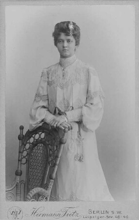 Porträt einer jungen Frau : Junge Frau, die an einem Stuhl lehnt. Fotografie (Carte-de-visite mit Atelieraufdruck verso) aus dem Warenhaus Hermann Tietz. Eigenes Atelier für Photographie