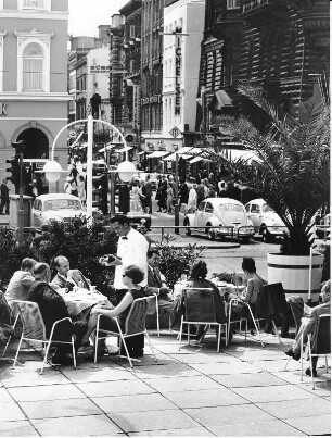 Hamburg-Neustadt. Gäste sitzen vor dem Alsterpavillon (Ferdinand Streb, 1953) am Jungfernstieg. Gegenüber ist die Einmündung der Straße Große Bleichen. Es herrscht starker Fußgängerverkehr