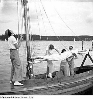 Segelschülerinnen auf einem Segelboot beim Versuch, ein Segel zu setzen