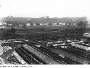 Blick vom Dach eines Hauses mit Giebelzier über eine Gärtnerei gegen eine Schachtanlage, wohl Nordböhmen