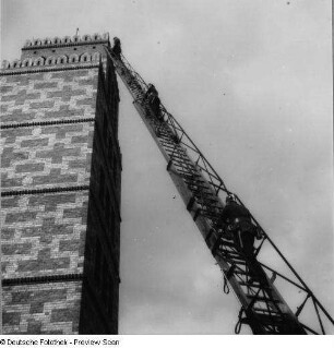 Berliner Feuerwehr. Feuerwehrleute beim Aufstieg auf einer an einen Schlauchturm angelegten Drehleiter