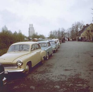 Weimar-Buchenwald. Nationale Mahn- und Gedenkstätte Buchenwald, Straße nach Weimar mit parkenden Autos, im Hintergrund Turm der Freiheit vom Mahnmal auf der Südseite des Ettersbergs (1954-1958)