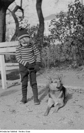 Ein Mädchen mit einem angeleinten Hund präsentiert einen winterlichen, zellwollenen Gamaschenanzug