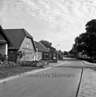 Dorfstraße: links und hinten rechts Einfamilien- und Bauernhäuser mit Vorgärten