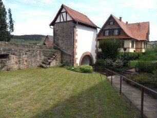 Kirchhof im Norden-Ansicht von Südwesten mit Torhaus (Romanisch) sowie im Westen anschließender Kirchhofmauer mit Treppe zum Wehrgang und erhaltenen Schießscharten in Brusthöhe