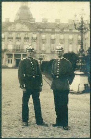 Zwei Uniformierte, im Hintergrund Schloß Karlsruhe.