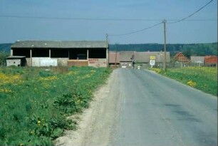 Ortseingangsstraße; im Hintergrund Ortsschild und Gebäude