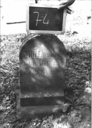 Grabstein 74 (Index: 100114058) Material: Sandstein Zustand: leicht verwittert Maße HxBxT: 56x34x18 cm Beschreibung: Stele, Sockel, Rundbogenabschluß Besonderheit: Kindergrab: Grabstein 74