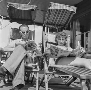 Elisabeth Gremmler und ein Mann lesen in Klappstühlen sitzend die Zeitschrift "Die neue Linie" und ein Buch