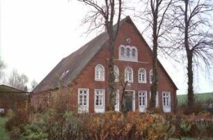 Klein Wesenberg (11): Bauernhaus aus Backstein: Giebelseite Wohntrakt mit Eingangstür, Sprossenfenstern, oben Bogenfenstern, mit Faschen: davor Bäume
