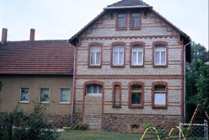 Giebelseite eines Hauses mit roten und hellen Steinen; Tür vermauert