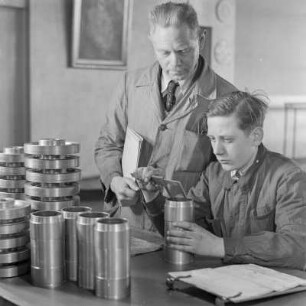 Lehrling bei Borgward misst ein Bauelement, der Ausbilder schaut zu