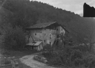 Mühle : Ein Mühlengebäude an einem Weg, an einem Hang gelegen.
