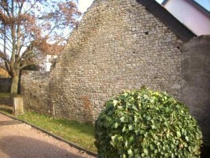 Kirchhof im Osten mit Kirchhofmauer als Außenwand eines angebauten Gebäudes (Wehrgang mit Steinbrüstung entfernt-beachte gezackte Giebelseite im Norden)