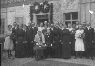 Hochzeitsgesellschaft vor einem Bauernhaus sitzend