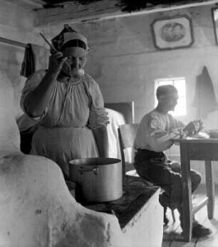 Bäuerin beim Kochen am Herd und Mann in der Küche