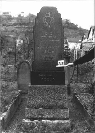 Grabstein 38 (Index: 99805055) Material: geschliffener Granit Zustand: leicht verwittert Maße HxBxT: 200x68x30 cm Beschreibung: Stele auf gestuftem Sockel mit gestuft eingezogenem abgeflachten Rundbogen Symbolik: Blumen im Giebel: Grabstein 38