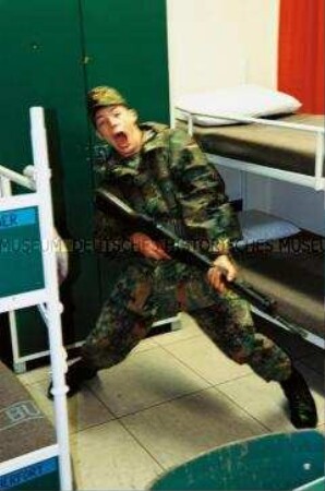 Wehrdienstleistender mit seinem Maschinengewehr im Zimmer (Altersgruppe 18-21)