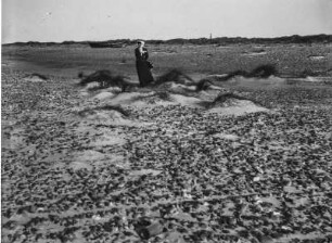 Frau zwischen Dünen : Blick auf kleine Dünen, dazwischen eine Frau stehend.