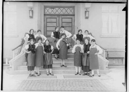 Haushaltungsschule in Gammertingen 1931; Junge Frauen mit Schürzen bei einer Aufführung mit Geigenspielerin auf einer Treppe vor dem Hauseingang
