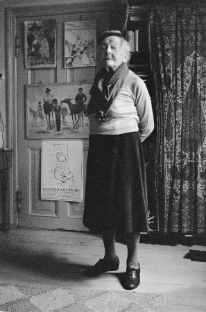 Die Malerin Charlotte E. Pauly in ihrer Wohnung, im Hintergrund u.a. ein Ausstellungsplakat von Dieter Goltzsche