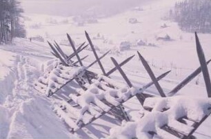 Blick auf eine Ortschaft im Erzgebirge im Winter mit einem Schneezaun im Vordergrund