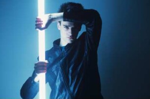 Neon : Mann in Lederjacke, en face, eine Neonröhre vor sich haltend