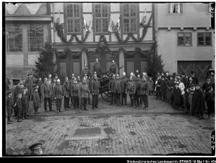 Übungen der Wolfenbütteler Freiwilligen Feuerwehr Enthält: Gruppe von Feuerwehrleuten vor einem geschmückten Fachwerkhaus mit dem Emblem "50", daneben Zuschauer