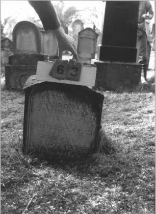 Grabstein 63 (Index: 99786687) Zustand: Inschrift oben rechts abgebrochen, z. T. verwittert, leicht eingesunken Maße HxBxT: 60x55x20 cm: Grabstein 63