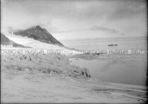 Schneebedeckte, zerklüftete Berglandschaft am offenen Meer, Dampfer in der Ferne, Nordlandreise, Norwegen