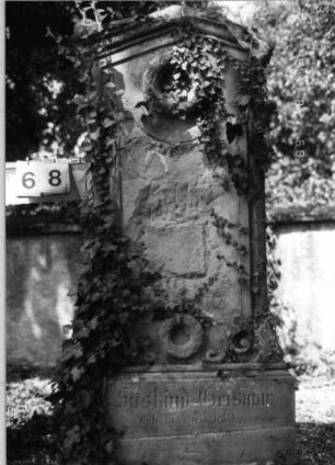 Grabstein 68 (Index: 100086526) Material: Sandstein Zustand: verwittert, Schriftplatte herausgeschlagen Maße HxBxT: 174x64x30 cm Beschreibung: Stele, Sockel, giebelartiger Abschluß Symbolik: zwei Kränze: Grabstein 68