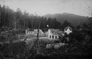 Grabkreuz vor kriegszerstörtem Haus