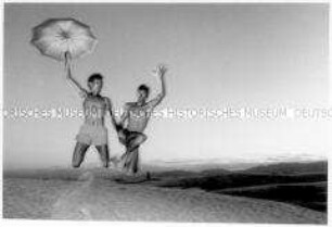 Zwei junge Männer in Shorts im Sprung mit einem aufgespannten Regenschirm in der Hand (Sonderthema: Traum-Bilder)