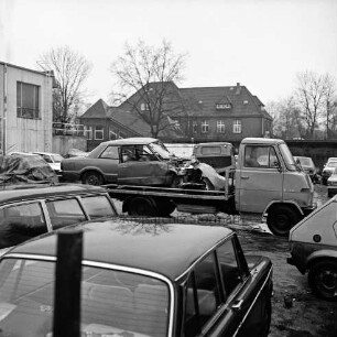 Hof des Abschleppdienstes am Waldemar-Bonsels-Weg: nach Verkehrsunfall: Wrack von Unfall-Pkw auf Plattform von Abschleppwagen: rundum abgestellte Pkws: hinten links: Werkstattgebäude, hinten Mitte: U-Bahnhof Ahrensburg West