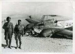 Zwei italienische Carabinieri der libyschen Infanterie bewachen eine in der Wüste abgestürzte Messerschmitt