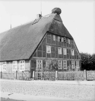 Dorfstraße mit Kopfsteinpflaster: Fachwerkbauernhaus Hans Martens mit Reetdach und Storchennest: rechts Garten: davor Zaun